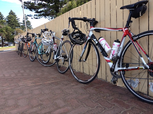 The peleton's bikes resting on a fence outside the bakery.