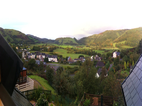A valley with a watercourse running through it makes its way to the sea. The edge of a town is visible on the left bank. Near the river are emerald green pastures. The low hills on both sides hold darker green forests.