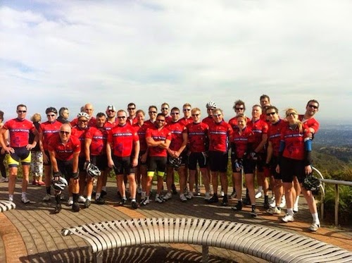 About 30 cyclists in red jerseys pose at the top of Mt. Lofty in the Aidelaide Hills. A patch on the fron of each jersey says Ride for Recovery.